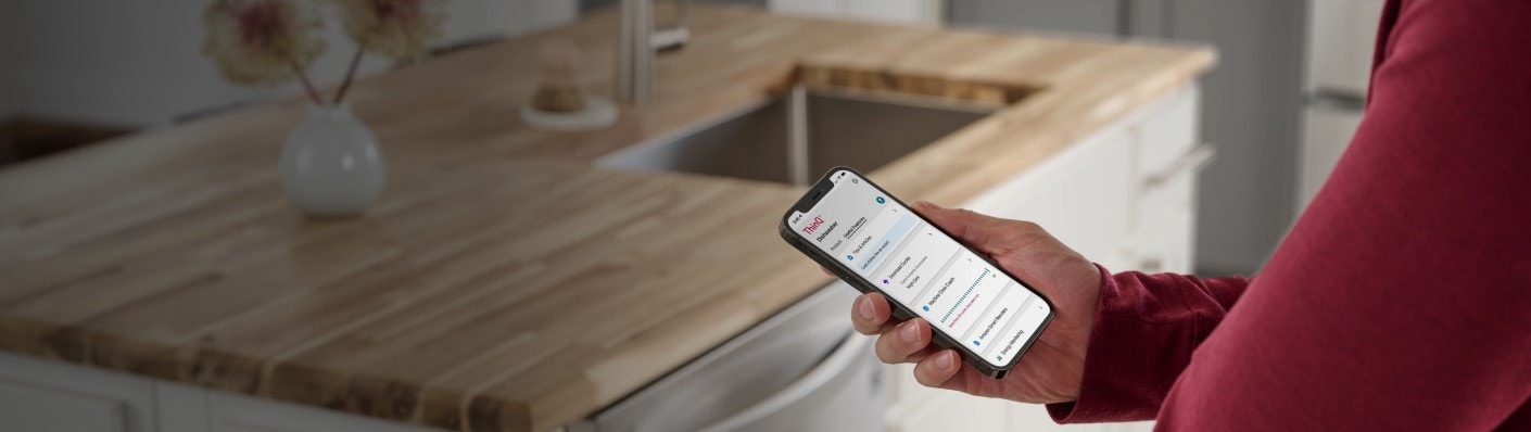 Hand holding a phone with the ThinQ app on the screen and the kitchen counter in the background.