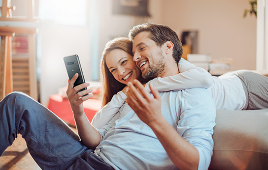 Пара обнимается и улыбается, смотря на экран смартфона.