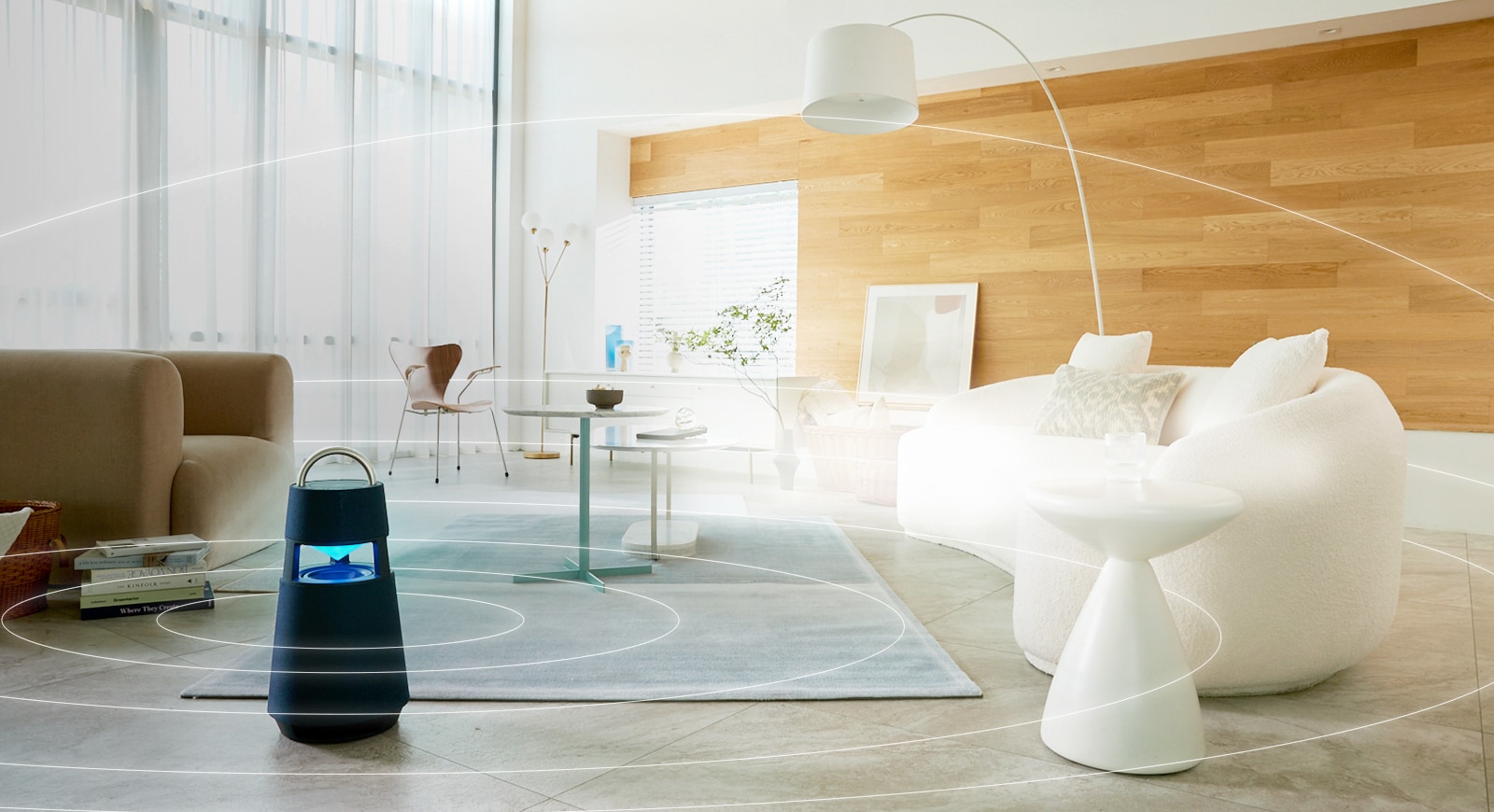 Hình ảnh các sóng âm thanh đang lan tỏa xung quanh chiếc loa XBOOM 360 được đặt trên sàn của căn phòng khách theo phong cách tối giản.