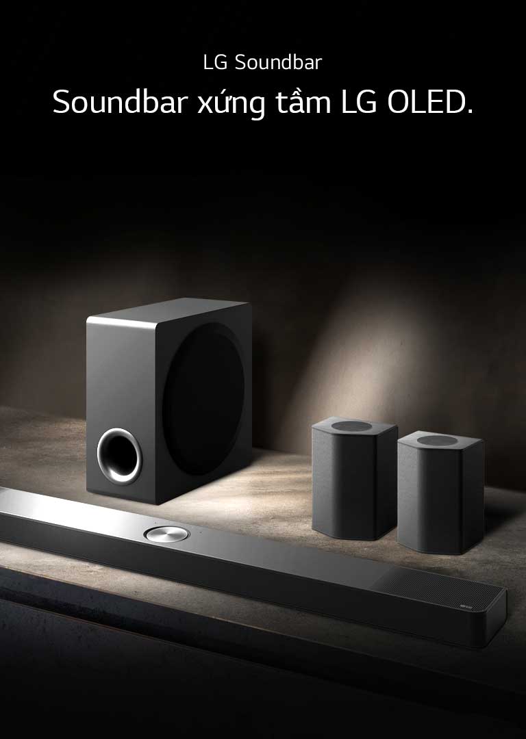 LG Soundbar, loa sau và loa siêu trầm được đặt trong phối cảnh góc nghiêng trên kệ gỗ màu nâu trong căn phòng màu đen, toàn bộ phòng chìm trong bóng tối với ánh sáng chỉ chiếu lên hệ thống âm thanh.
